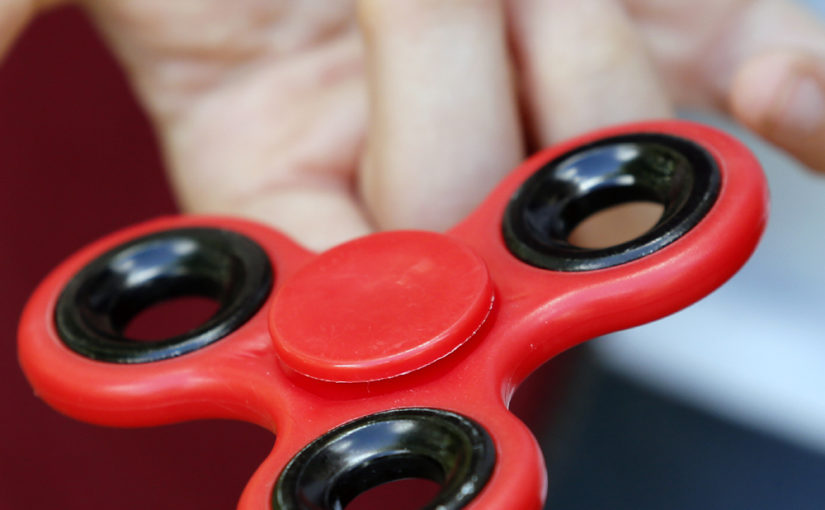 A close up of a tri-style fidget spinner balanced on a finger.